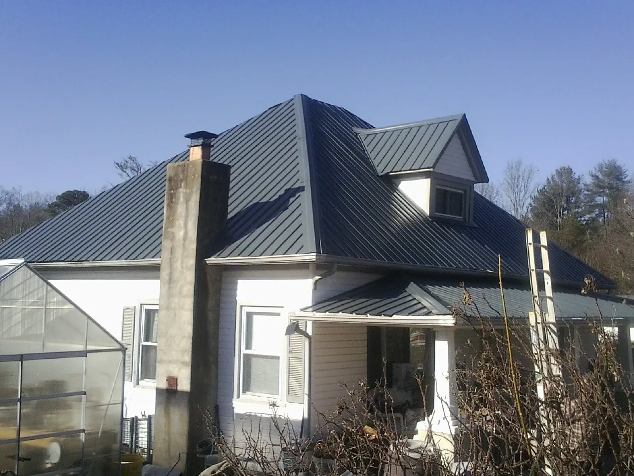 Dark blue standing seam metal roof on a white farmhouse with dormer — Slate & Tile Roof Repair by Roofing Brothers in Blooming Grove