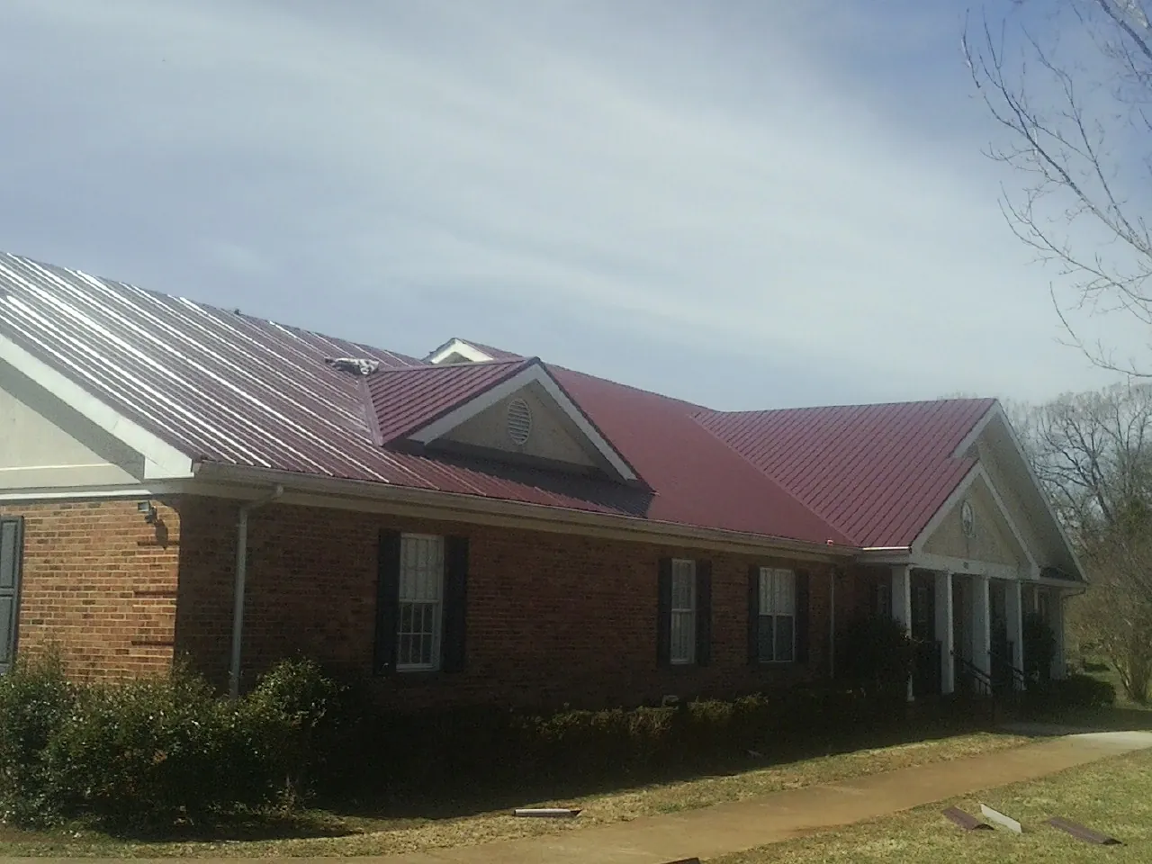 Red metal roof with gabled entries on a long brick building, from a Hail Damage Roof Repair job in Blooming Grove