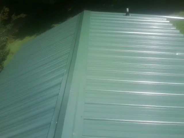 New green metal panels meeting at the ridge of a roof — Flat Roof Repair work by our crew in Blooming Grove