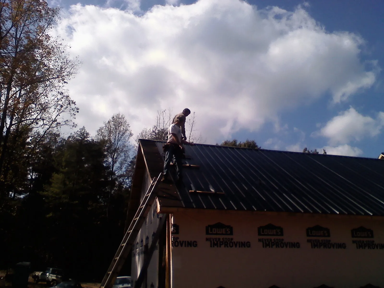Roofer fastening dark metal panels high against a cloudy sky, from a Roof Inspection job in Blooming Grove