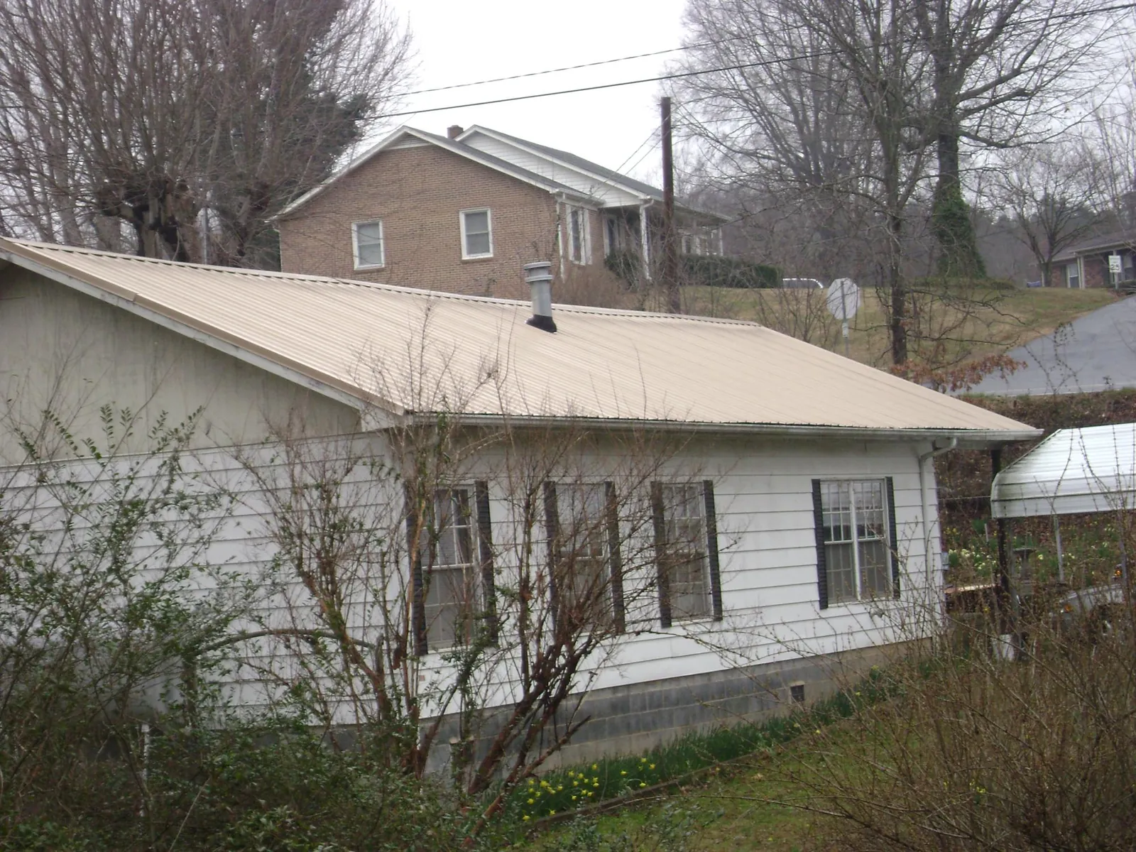 Tan metal roof on a white sided house set into a hillside — Commercial Roofing by Roofing Brothers in Blooming Grove
