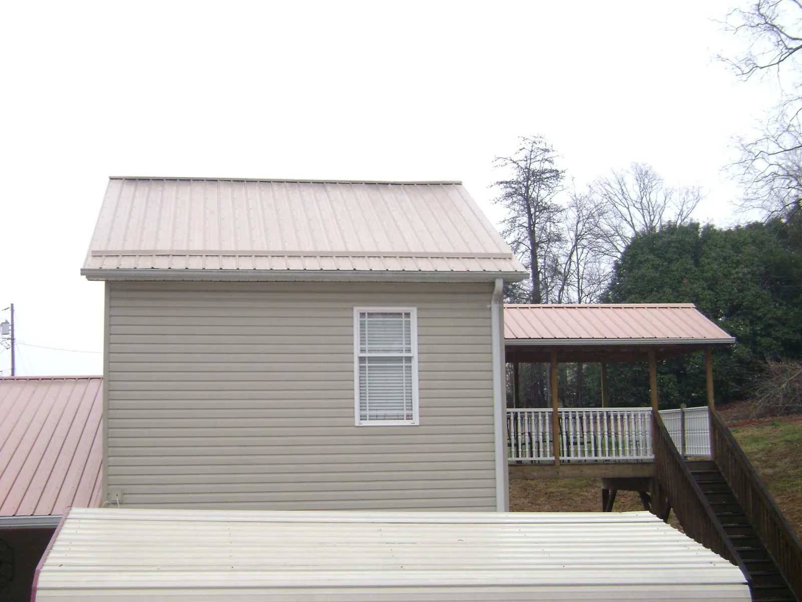Tan metal roofs on a two story addition and attached porch, from a Roof Replacement job in Blooming Grove